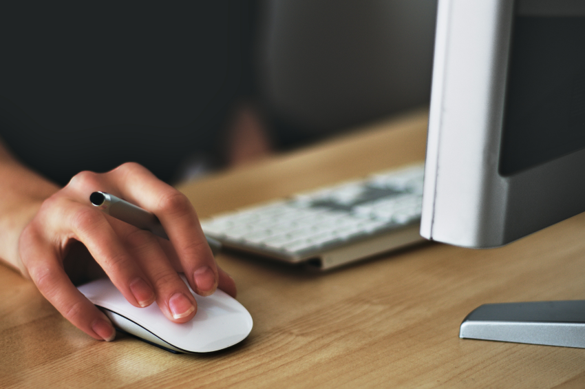 Hand holding a pen between fingers clicking on a computer mouse