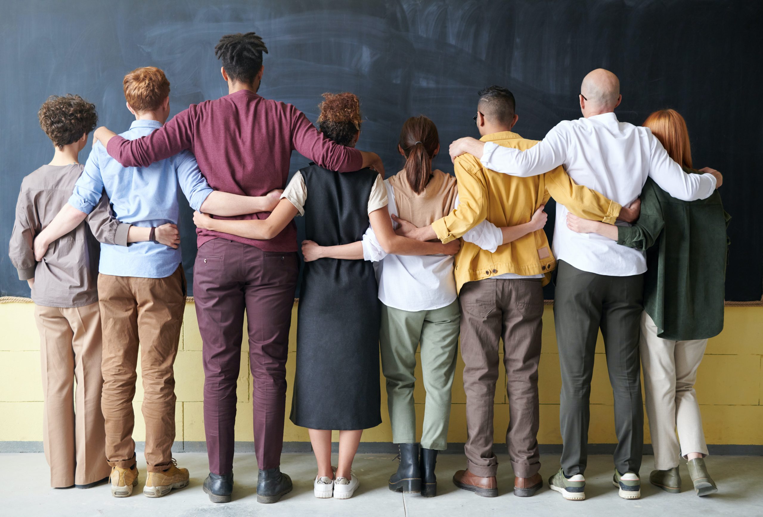 Group of teachers and students holding each other facing a chalkboard