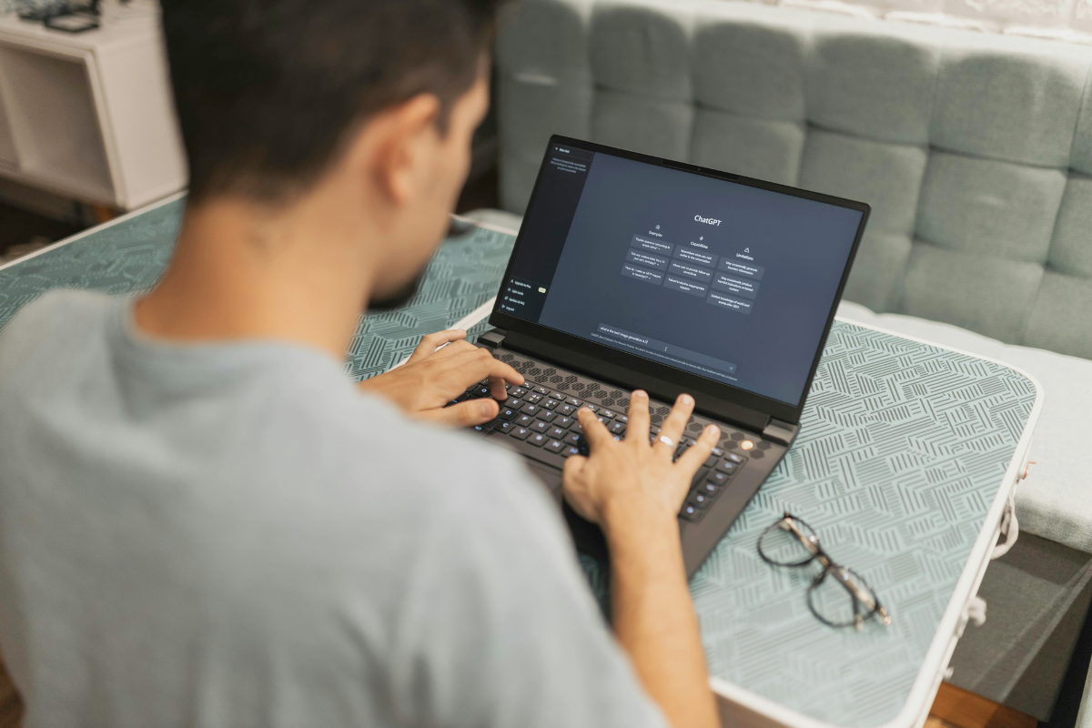 Student typing on a laptop using AI tutor with a dark screen showing charts or code while sitting at a table in a modern room.