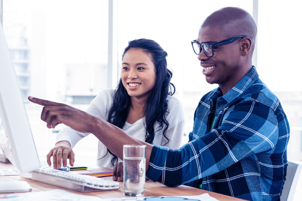 A female student sitting at desk with a male student pointing at a computer screen discussing accessibility in higher education.