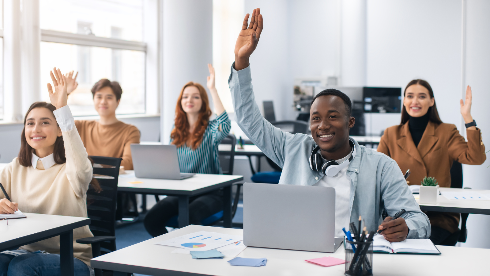 students in classroom with hands raised and laptops learning through evidence-based teaching practices